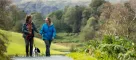 Two visitors walking a dog on a path at Tarn Hows in Cumbria