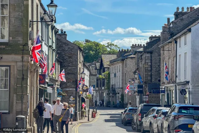 Kirkby Lonsdale town centre with stone buildings, flags and visitors on a sunny day